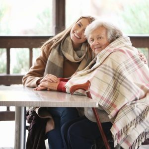 Senior woman and young caregiver sitting at table in cafe